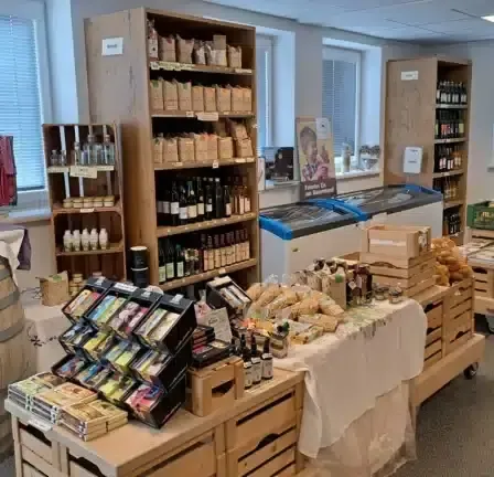 Ein gut bestückter Laden mit Holzregalen, gefüllt mit verschiedenen Produkten, einem Fass und einem Tisch mit einem weißen Tuch. Der Laden hat ein modernes Design mit weißen Wänden und Fenstern.