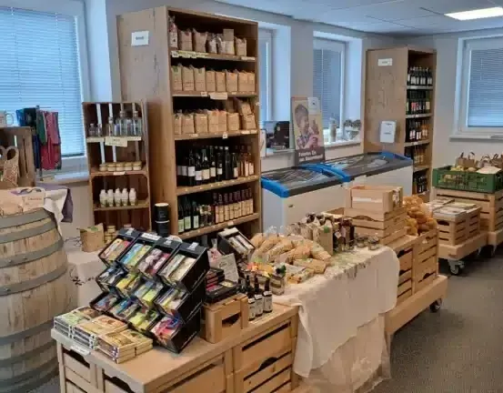 Ein gut bestückter Laden mit Holzregalen, gefüllt mit verschiedenen Produkten, einem Fass und einem Tisch mit einem weißen Tuch. Der Laden hat ein modernes Design mit weißen Wänden und Fenstern.