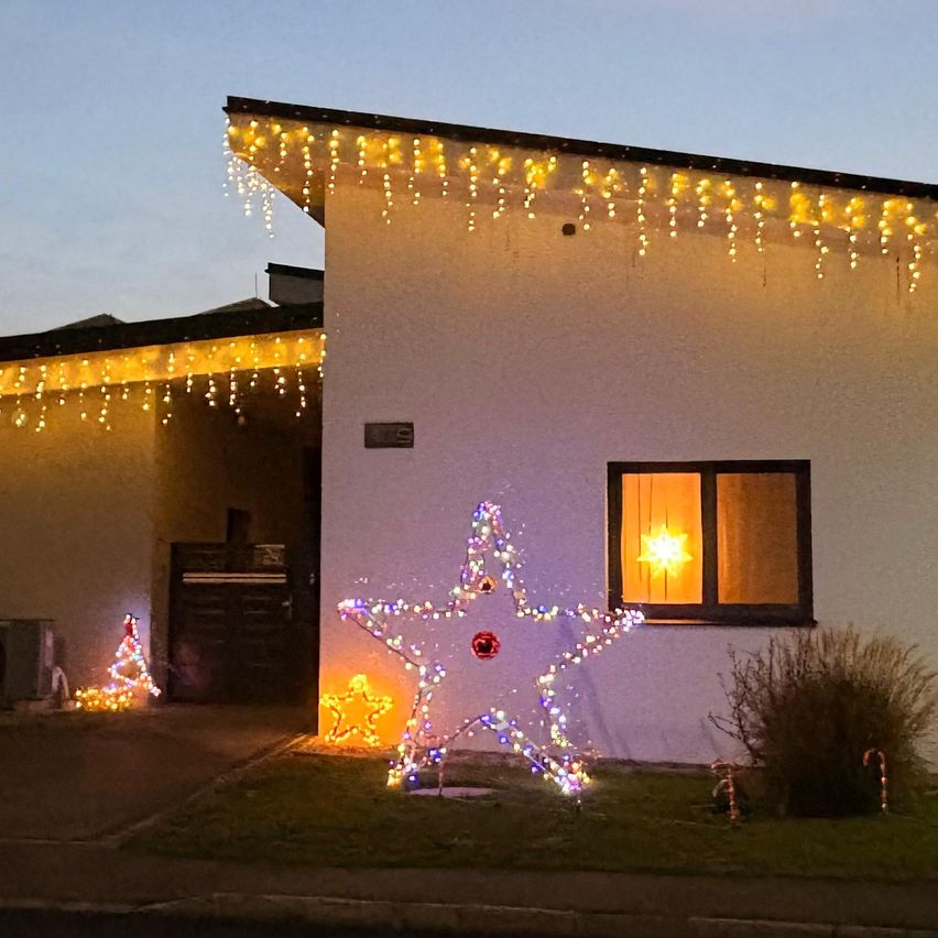 Ein Haus ist für Weihnachten mit Lichterketten und einem großen Stern im Vorgarten geschmückt. Das Haus hat ein Fenster mit einem leuchtenden Stern im Inneren.