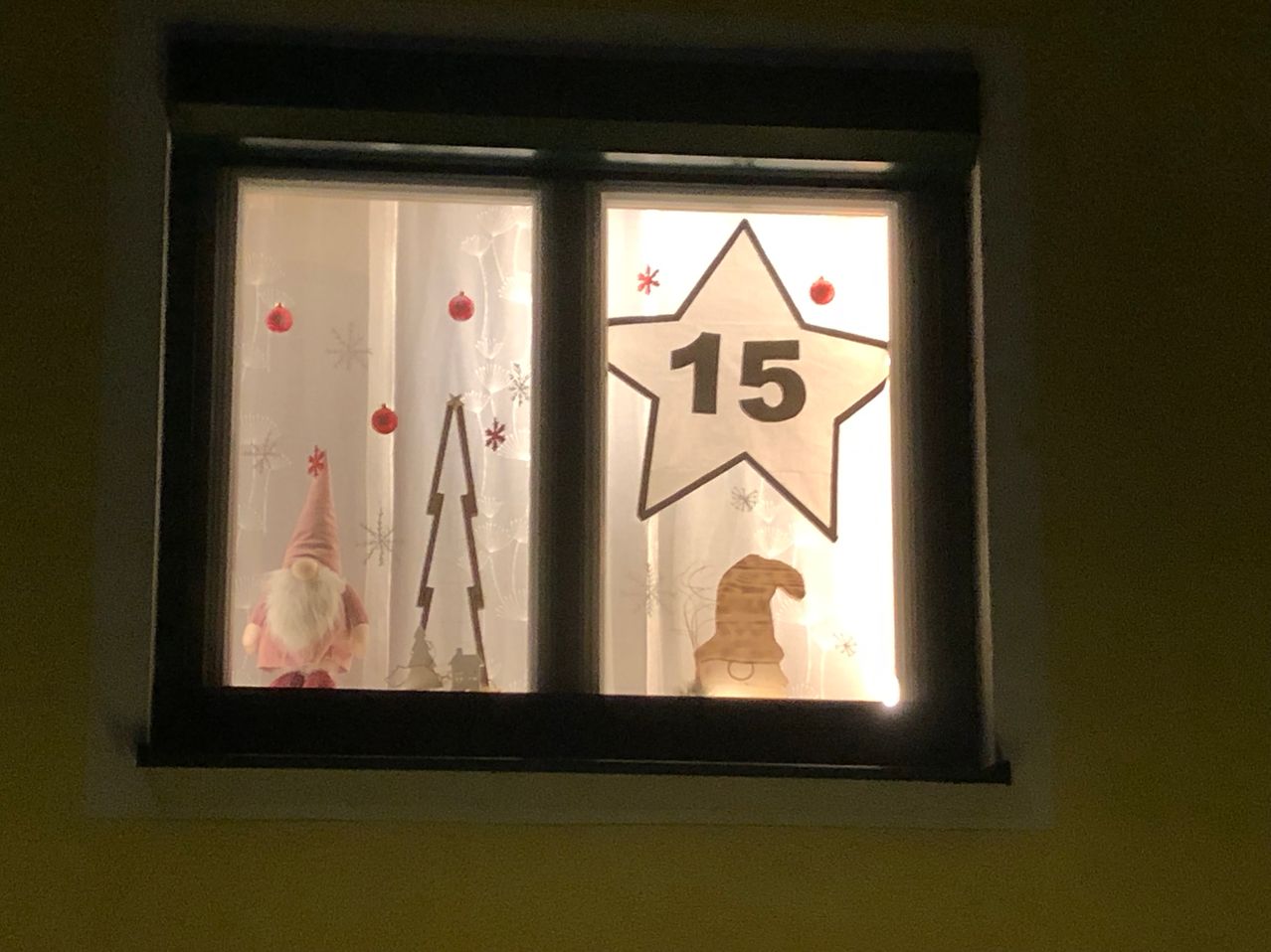 Ein Fenster mit Weihnachtsdekoration: ein Gnom, ein Weihnachtsbaum, Schneeflocken und ein Stern mit der Nummer 15.