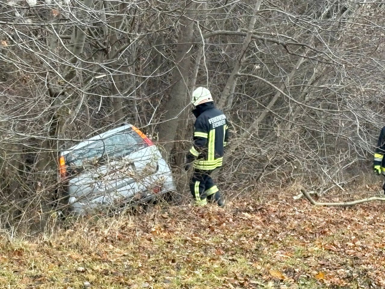 Ein Feuerwehrmann steht neben einem im Gebüsch feststeckenden Auto. Der Stoßfänger des Autos ist beschädigt.