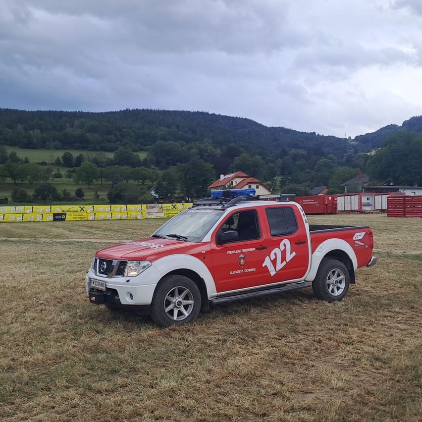 A red and white truck with the number 122 is parked in a field with mountains in the background.