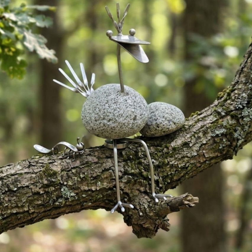 Eine metallische Vogelskulptur aus Steinen und Metall sitzt auf einem Ast in einem Wald.