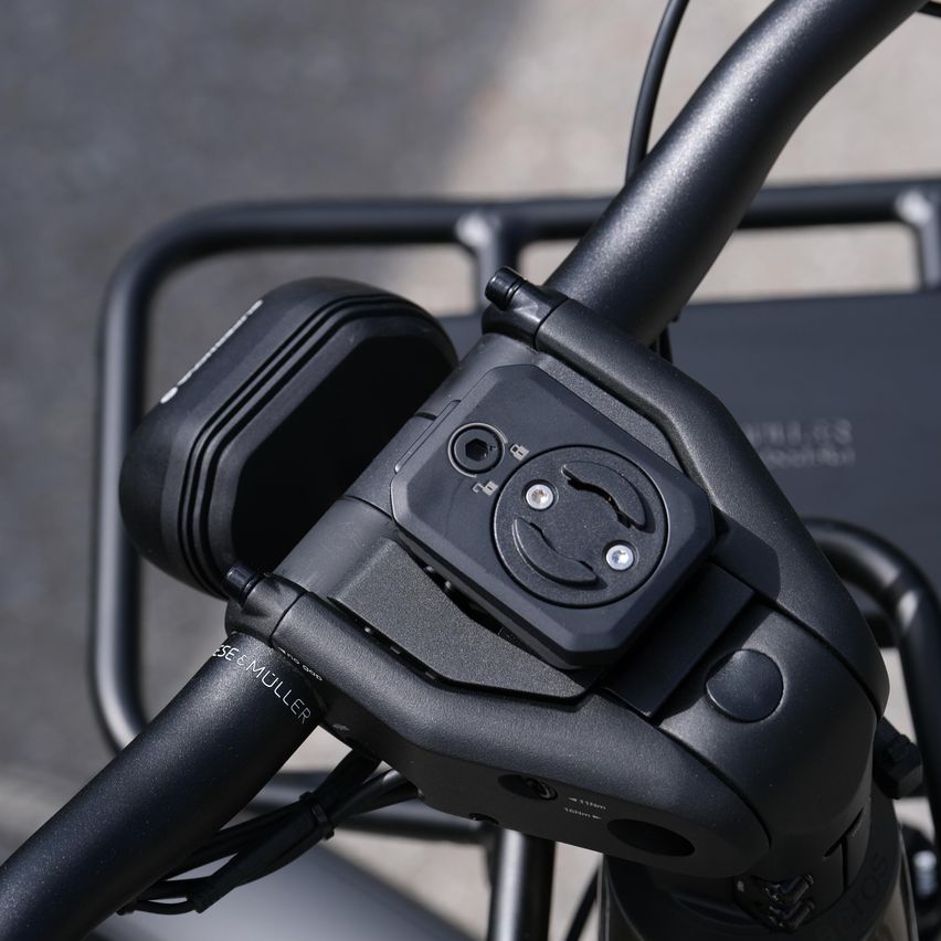 Nahaufnahme eines Fahrradlenkers mit einem schwarzen Gerät. Das Gerät hat ein lächelndes Gesicht, eine Kamera und einen runden Knopf. Der Lenker hat auch eine Metallstruktur und einen schwarzen Griff.