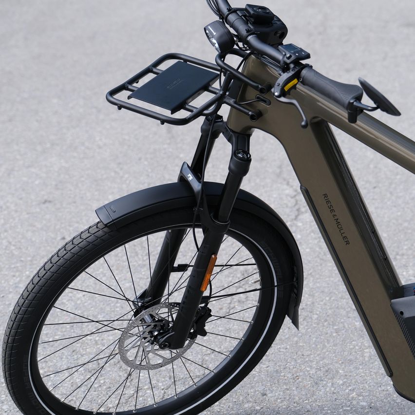 Nahaufnahme des Vorderrads und der Lenker eines Elektrofahrrads. Das Fahrrad hat eine schlanke, matte grüne Oberfläche und ein montiertes Tablet.