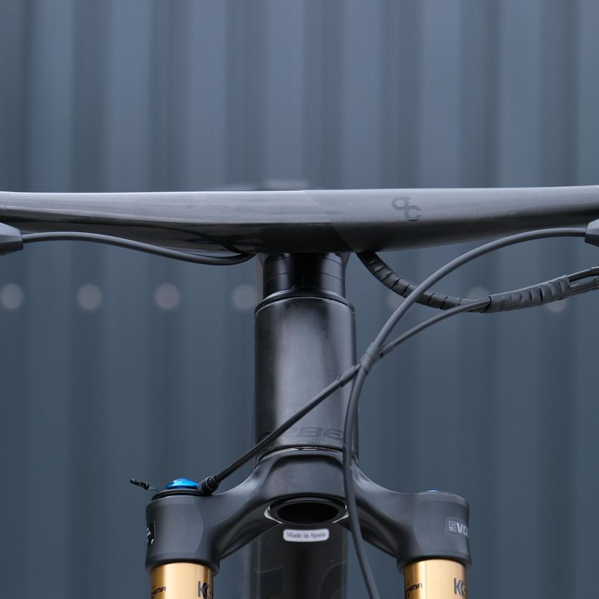 Nahaufnahme eines schwarzen Fahrrad-Vordergabel mit goldenen Akzenten auf grauem Hintergrund. Die Gabel ist mit verschiedenen Kabeln und Komponenten ausgestattet.