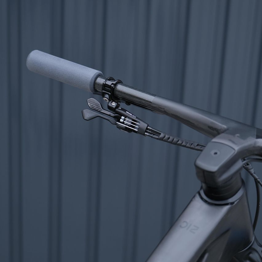 Nahaufnahme der Fahrradlenker mit Griff und Bremshebel, vor grauem Hintergrund.