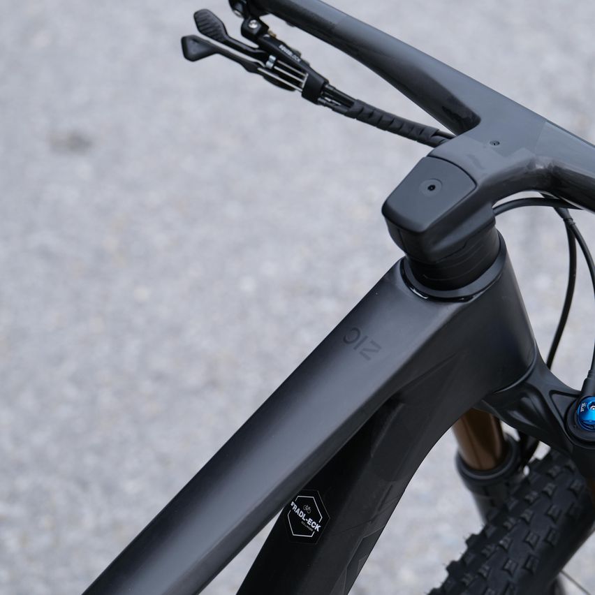 Eine Nahaufnahme eines schwarzen Fahrradlenkers, mit dem Wort 'RIDE' auf dem Rahmen eingraviert. Der Lenker ist mit einem blauen Knopf am Fahrrad befestigt.