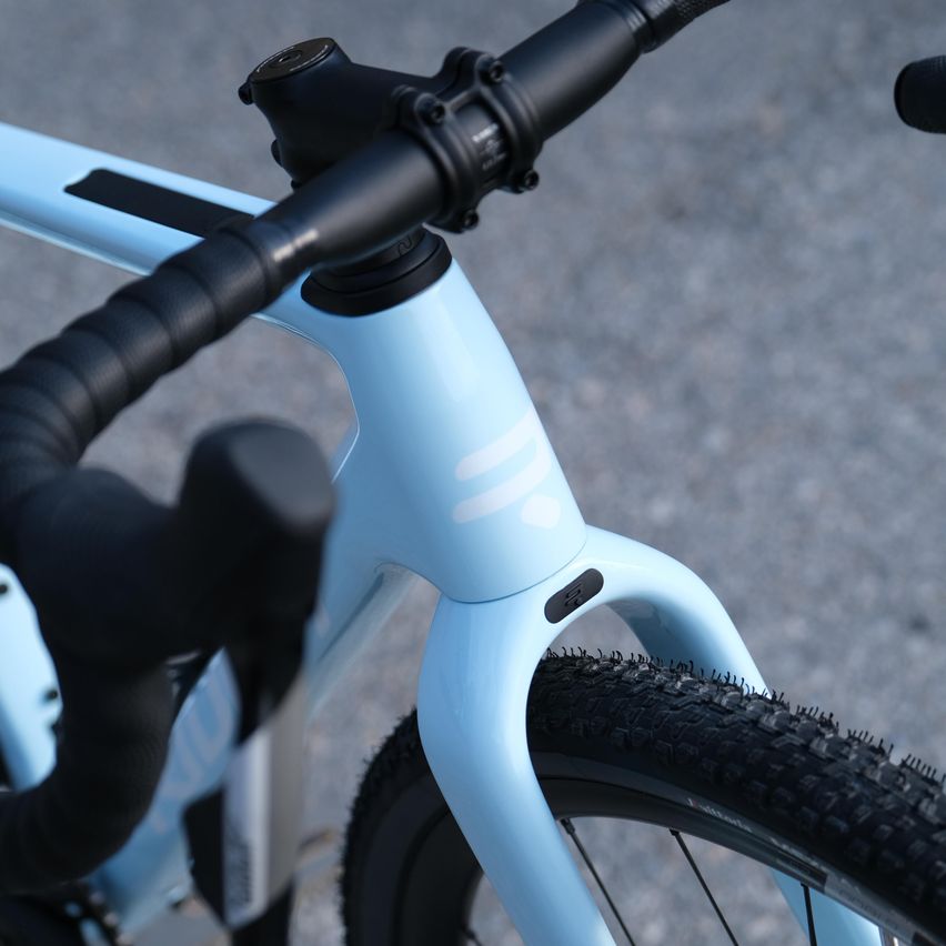 Eine Nahaufnahme eines blauen Fahrrads mit schwarzen Lenkern und einem Knauf am Unterrohr. Das Fahrrad hat einen schwarzen Sattel und Pedale.