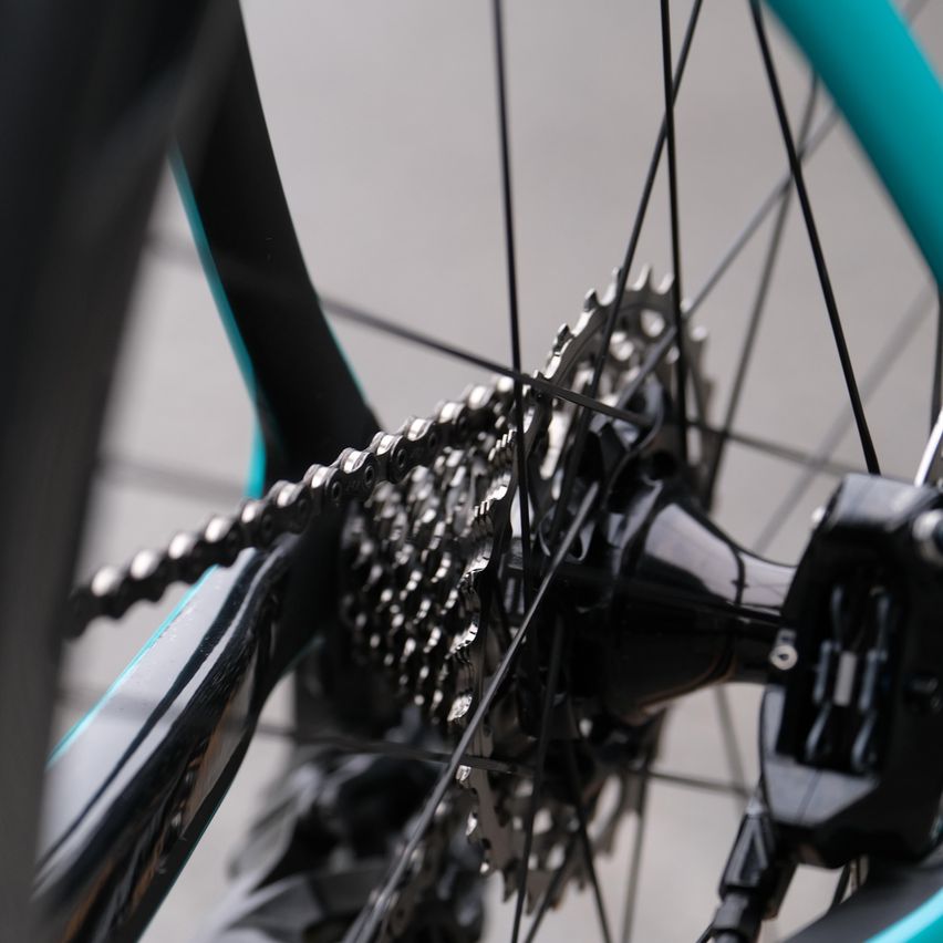 Nahaufnahme des Hinterrads eines Fahrrads, das die komplizierte Kette und Kettenräder zeigt. Der Rahmen des Fahrrads hat ein schlankes schwarzes und türkisfarbenes Design.