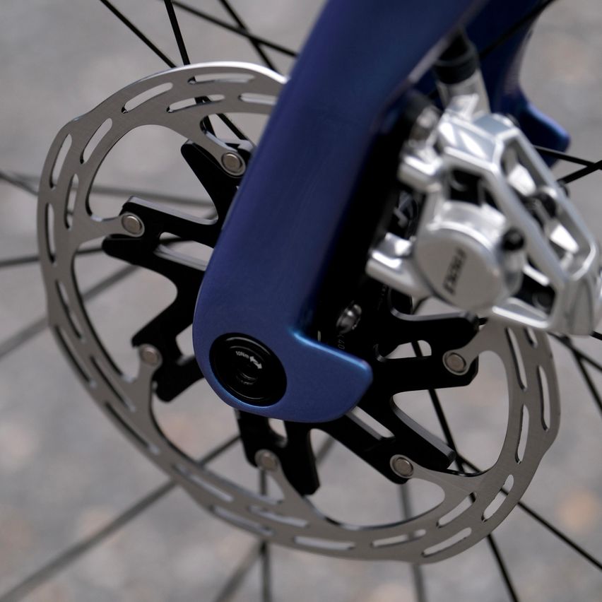 Eine Nahaufnahme des Vorderrads eines Fahrrads zeigt den blauen Rahmen, die silberne Scheibenbremse und die schwarzen Speichen.