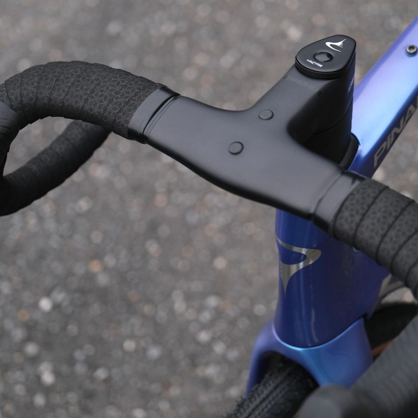 Nahaufnahme der schwarzen Griffe und blauen Lenker eines Fahrrads. Der Rahmen hat einen silbernen Akzent und die Lenker schwarze Knöpfe.