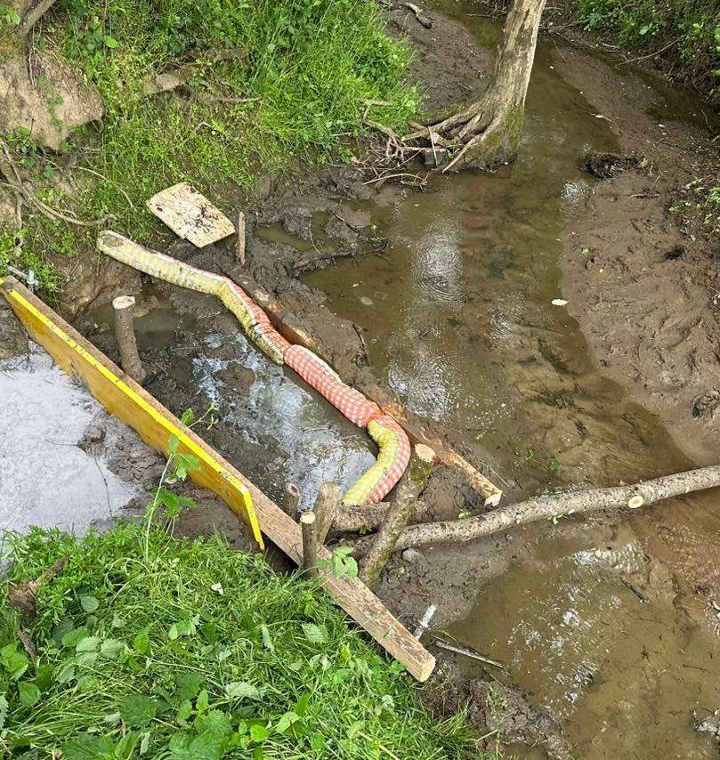 Ein schlammiger Bach mit freiliegenden Rohren und Holzpfählen, wahrscheinlich ein Wassermanagement-Element oder eine Reparatur.