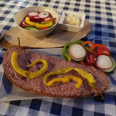 Ein Teller mit einem Stück Fleisch, gelben Paprikastreifen und einem Salat mit Gemüse auf einem blau-weiß karierten Tischtuch.