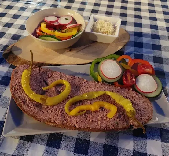 Ein Teller mit einem Stück Fleisch, gelben Paprikastreifen und einem Salat mit Gemüse auf einem blau-weiß karierten Tischtuch.