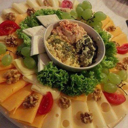 Eine Käseplatte umfasst eine Vielzahl von Käsesorten, Trauben, Salat und eine Schüssel Dip, alles auf einer Holzoberfläche angeordnet.