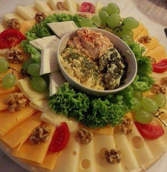 Eine Käseplatte umfasst eine Vielzahl von Käsesorten, Trauben, Salat und eine Schüssel Dip, alles auf einer Holzoberfläche angeordnet.