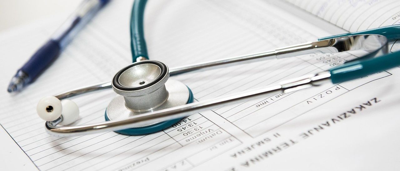 Ein Stethoskop liegt auf einem Patientenformular mit einem Stift in der Nähe. Das Formular enthält Felder für Patientendaten und Messungen.