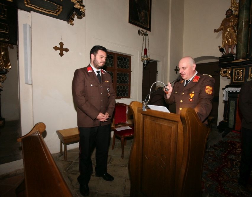 Zwei Männer in Militäruniformen stehen in einer Kirche. Ein Mann spricht in ein Mikrofon an einem hölzernen Podest.