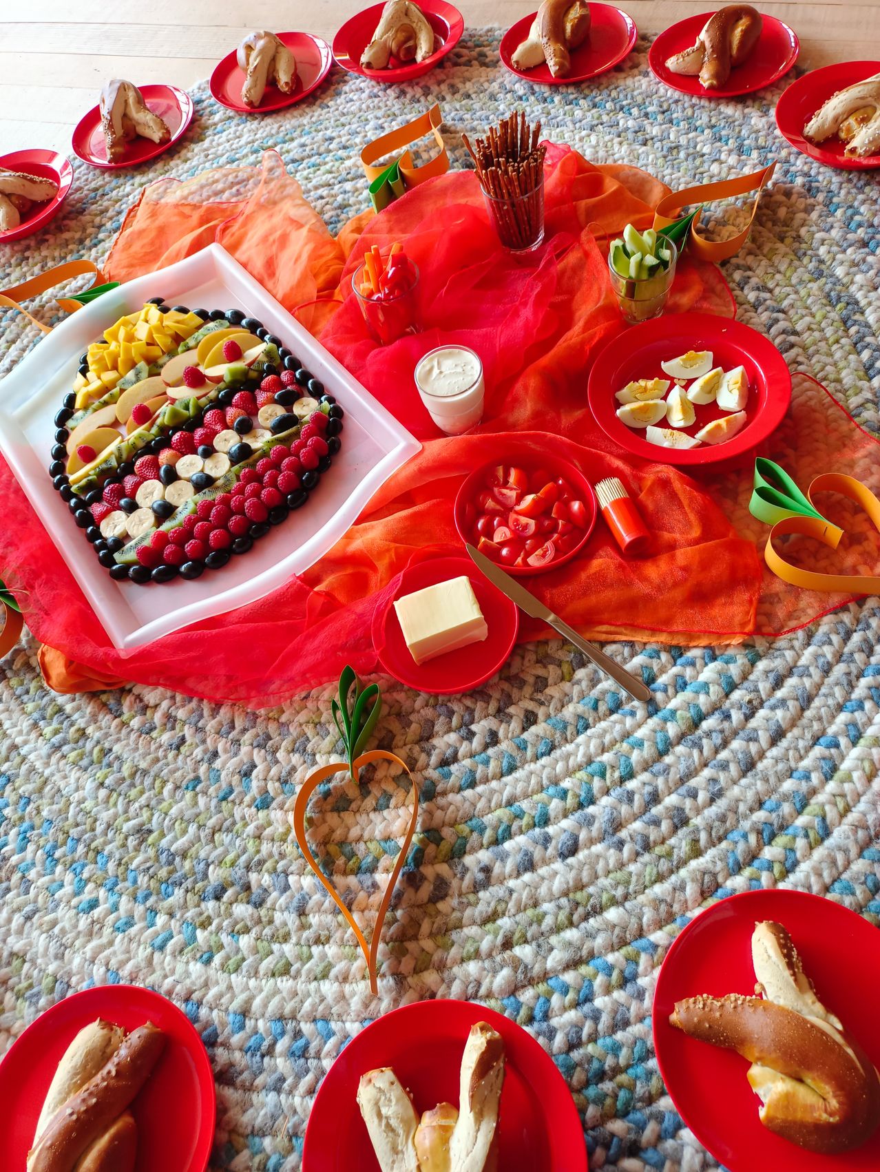 A heart shaped fruit platter with various fruits like mango, pineapple, banana, strawberries, and raspberries. There are also eggs, cheese, and vegetables like tomatoes.