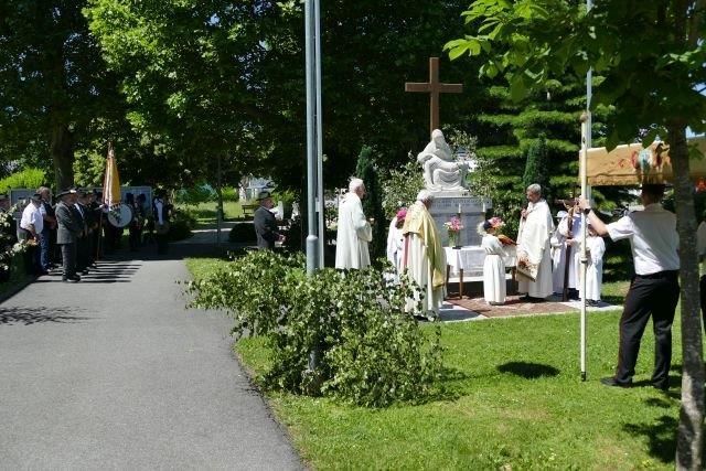 Religious clergy in white garments perform a ceremony near a large cross and altar, with attendees and a flag in the background.