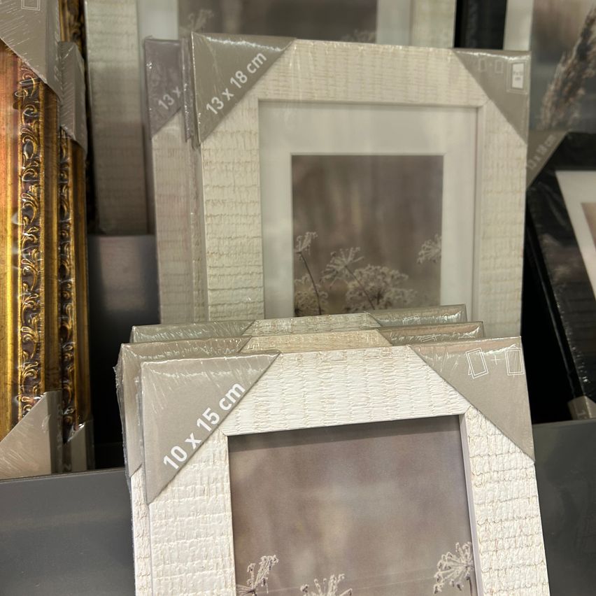 Gestapelte Bilderrahmen in verschiedenen Größen und Designs sind ausgestellt, wobei ein 13x18 cm und ein 10x15 cm Rahmen im Fokus stehen. Die Rahmen haben strukturierte Kanten und sind in weißen und goldenen Ausführungen.