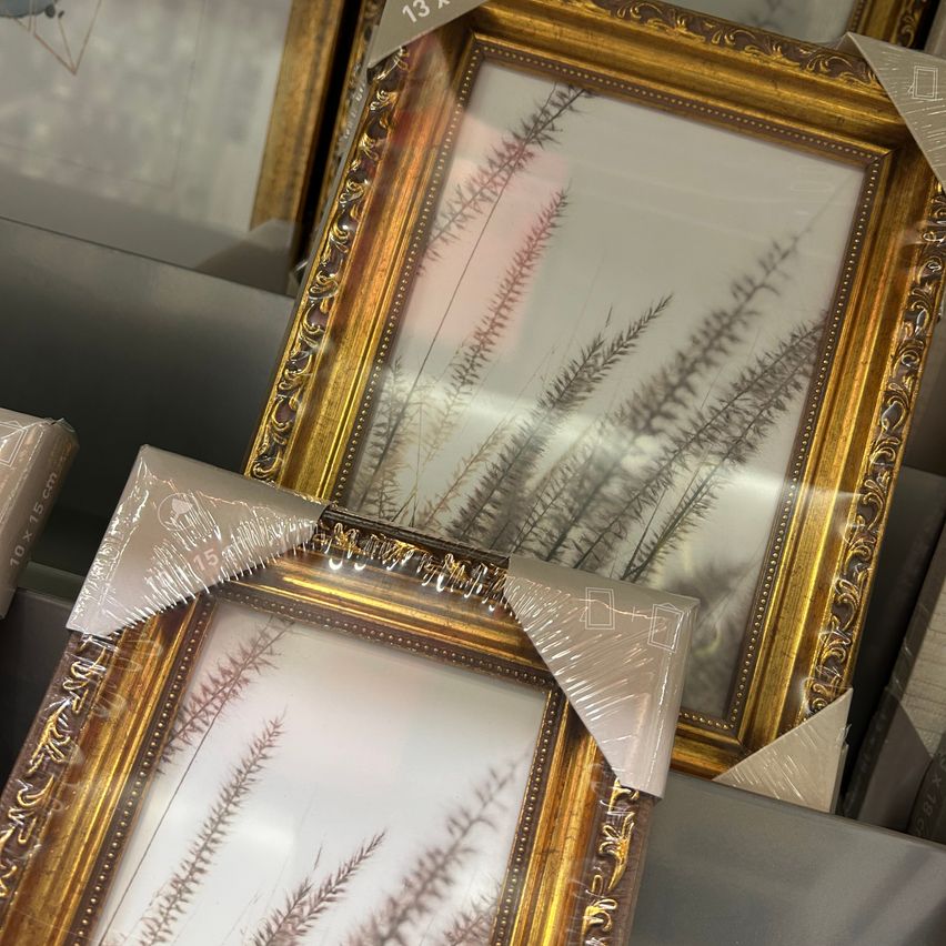 Gestapelte Goldrahmen-Bilderrahmen mit weißem Hintergrund und abstrakten pflanzenartigen Drucken. Ein Rahmen hat einen 13-Zoll-Aufkleber.