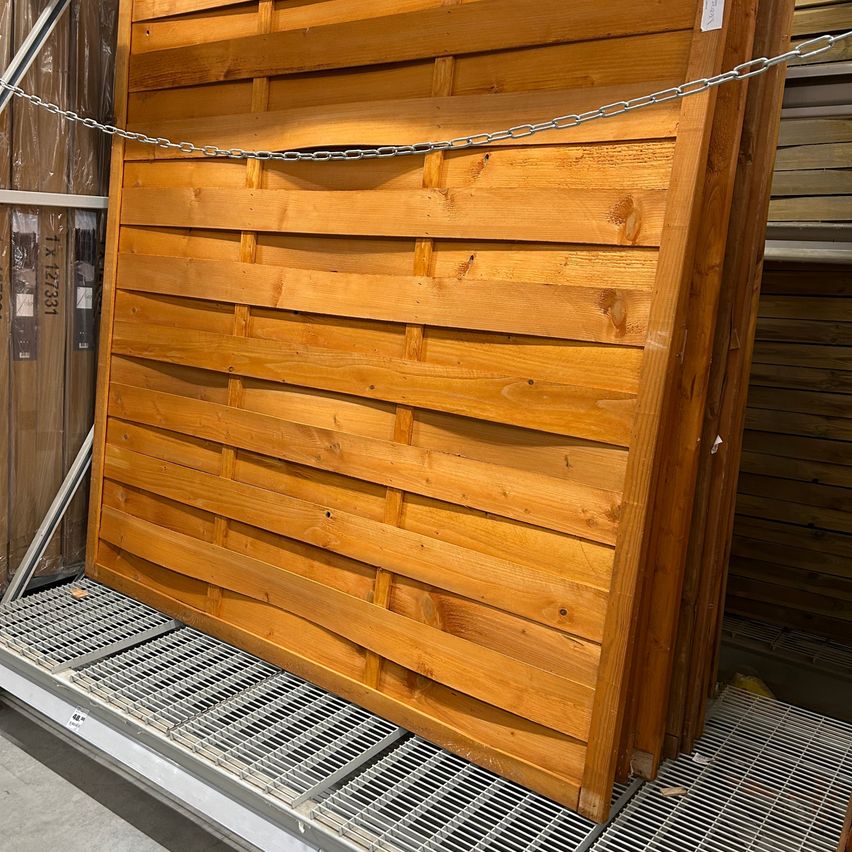 Ein Stapel von Holzlatten, der mit einer Kette gesichert ist und auf einem Metallrost ruht.