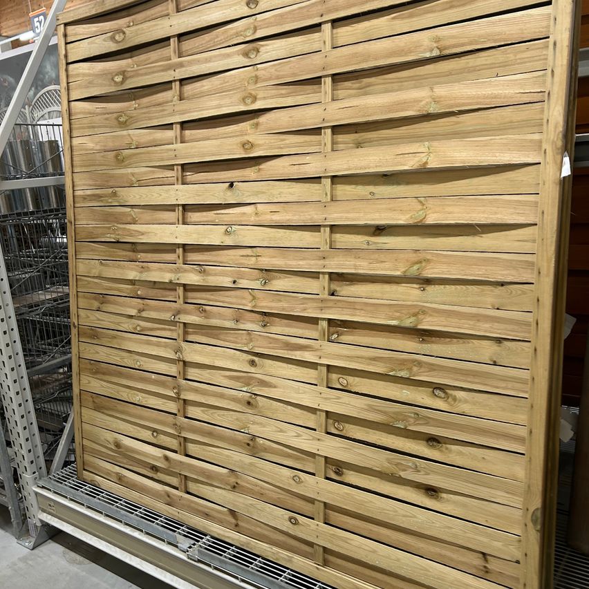 Eine Nahaufnahme einer Holzlatten-Gartenmauer. Die Mauer hat ein wellenförmiges Muster mit horizontalen und vertikalen Lamellen.