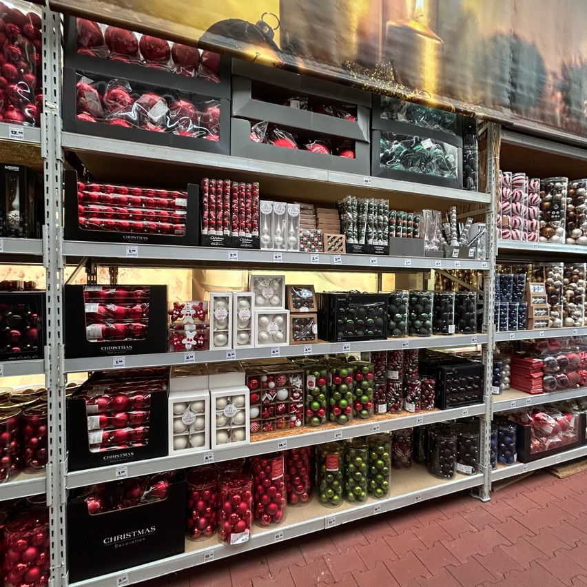 Ein Geschäft gefüllt mit Weihnachtsdekorationen, darunter rote und grüne Kugeln sowie verschiedene andere Artikel, alle ordentlich auf Regalen angeordnet.