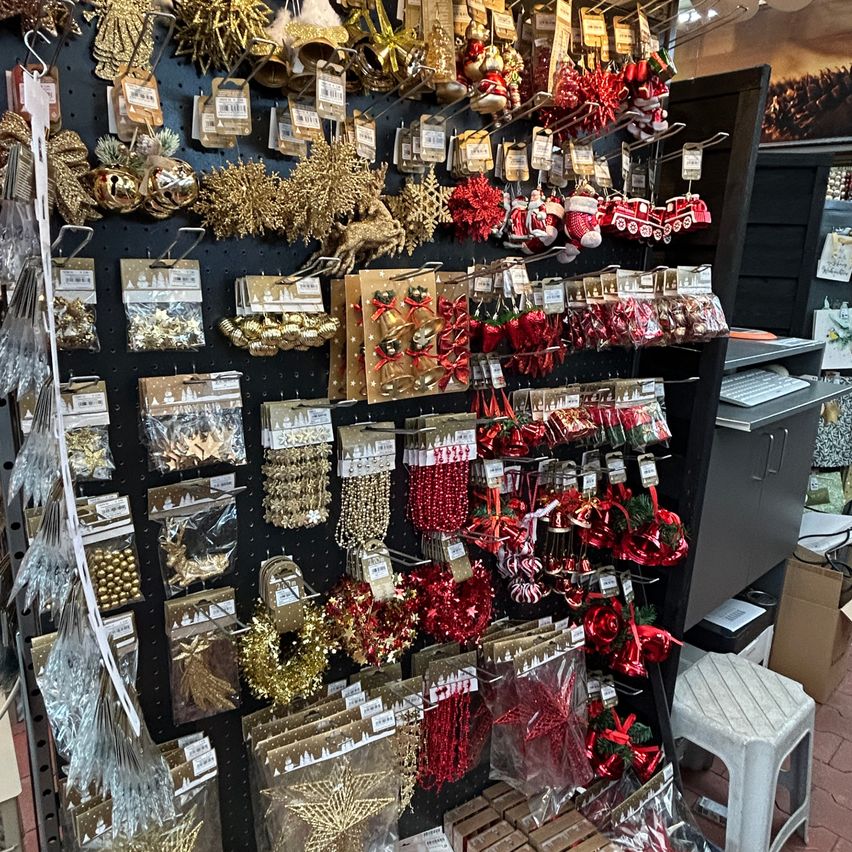 Ein Geschäft voller verschiedener Weihnachtsdekorationen, darunter rote und goldene Ornamente, Kränze und Girlanden. Die Artikel sind auf einem schwarzen Lochbrett ausgestellt.