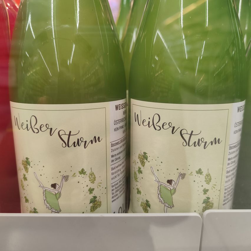 Two bottles of Weisser Sturm wine with a green label featuring a dancer and grapes on a store shelf.