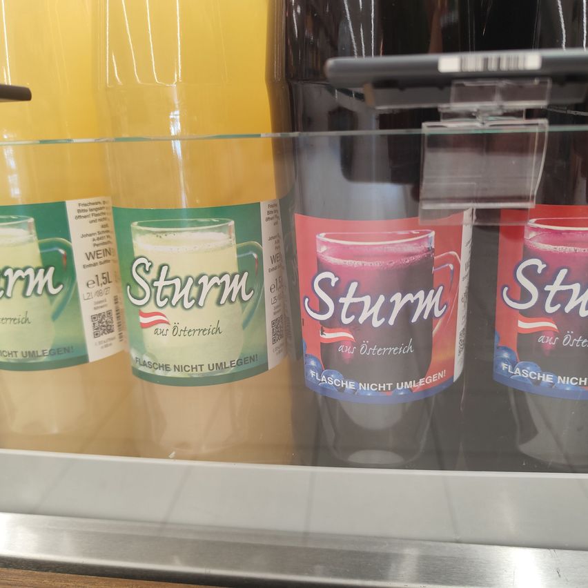 Four bottles of Sturm fruit juice in a glass display case. The bottles are transparent and contain different colored juices. The labels are green and white.