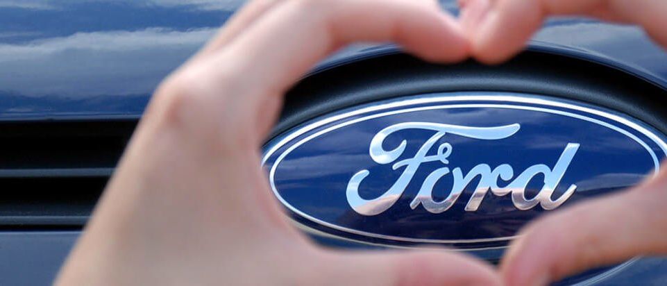 Eine Person formt mit den Händen ein Herz um das Ford-Logo auf einem Autogrill.