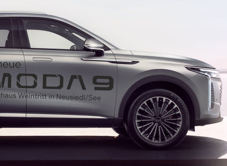 Ein silberner SUV mit dem Text 'Der neue OMODAD 9' an der Seite. Er steht auf einer schwarzen Oberfläche, möglicherweise in einem Autohaus.