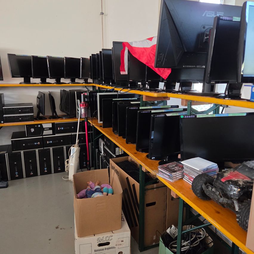 A room filled with various computer monitors, CPUs, and accessories on shelves. A box with stuffed toys sits on the floor.