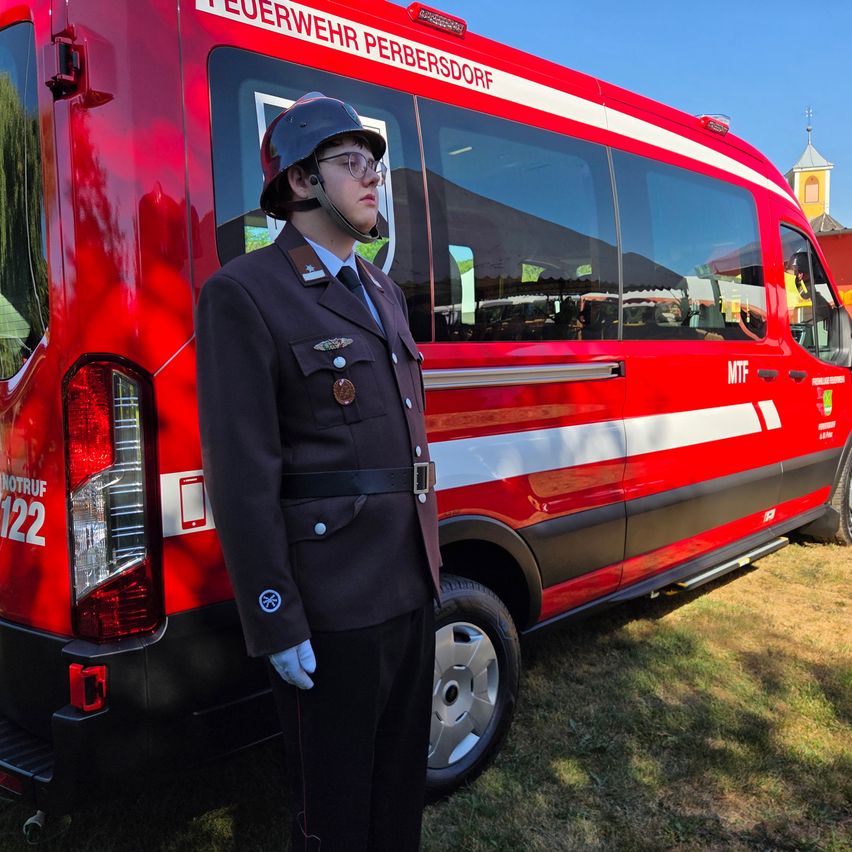 A firefighter in uniform stands in front of a red fire truck with the text 'Feuerwehr Perbersdorf' on the side.