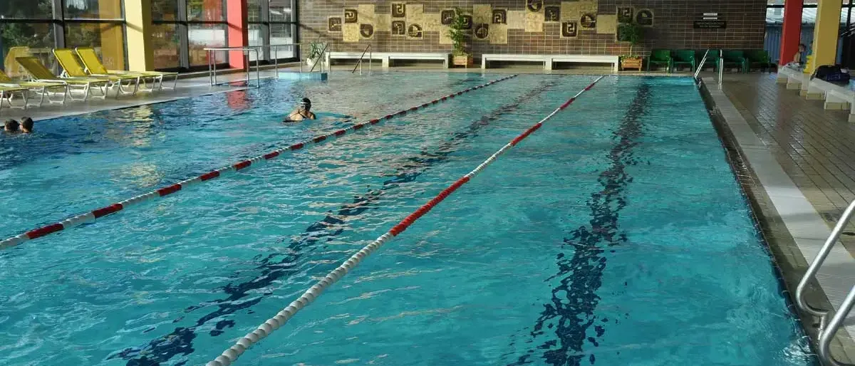 Ein Hallenschwimmbad mit blauem Wasser und einem Schwimmer, der eine Schwimmbrille und eine Schwimmmütze trägt. Der Pool hat rote und weiße Bahnmarkierungen.