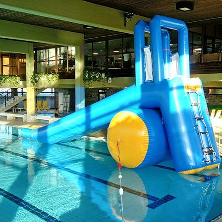 Ein großer aufblasbarer Wasserrutsche befindet sich in einem Poolbereich. Die Rutsche ist blau und gelb mit einer Leiter. Der Pool ist sauber und blau.