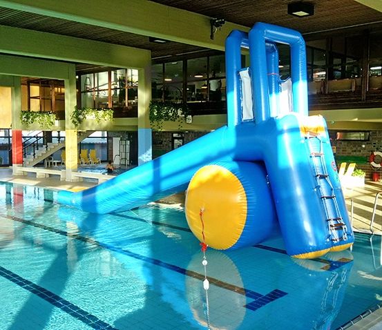 Ein großer aufblasbarer Wasserrutsche befindet sich in einem Poolbereich. Die Rutsche ist blau und gelb mit einer Leiter. Der Pool ist sauber und blau.