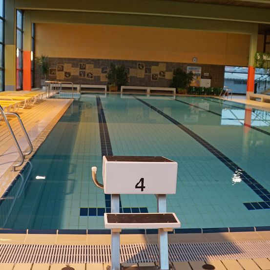 Ein Hallenbad mit blauen Fliesen und Bahnmarkierungen. Eine weiße Sprungbrett ist mit der Nummer 4 gekennzeichnet.