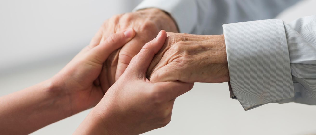 Eine Person hält die Hand einer älteren Person mit Fürsorge und Unterstützung.