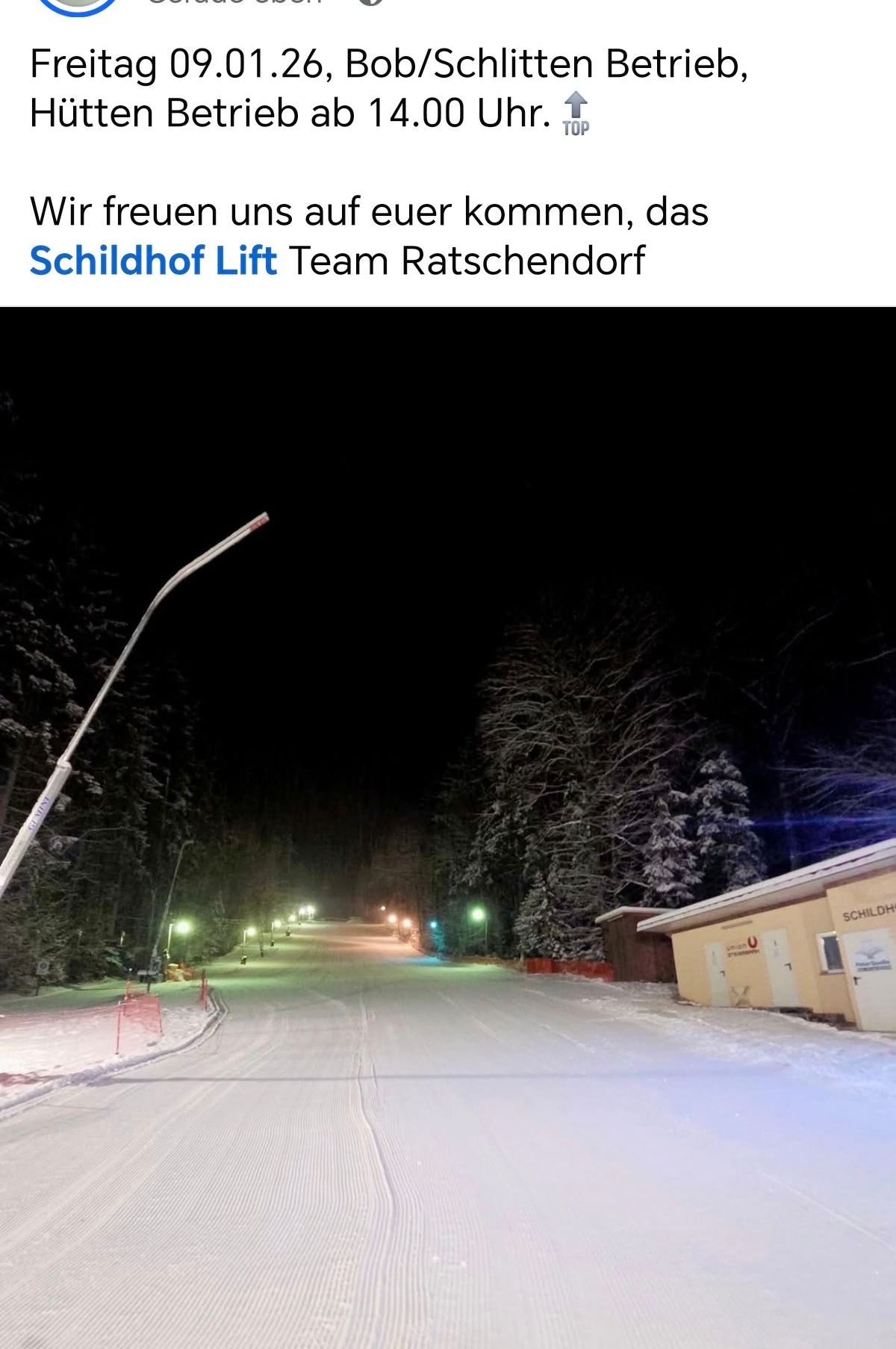 Eine verschneite Piste mit Straßenlaternen und einem Gebäude, das Schildhof Lift im Hintergrund beschriftet ist.