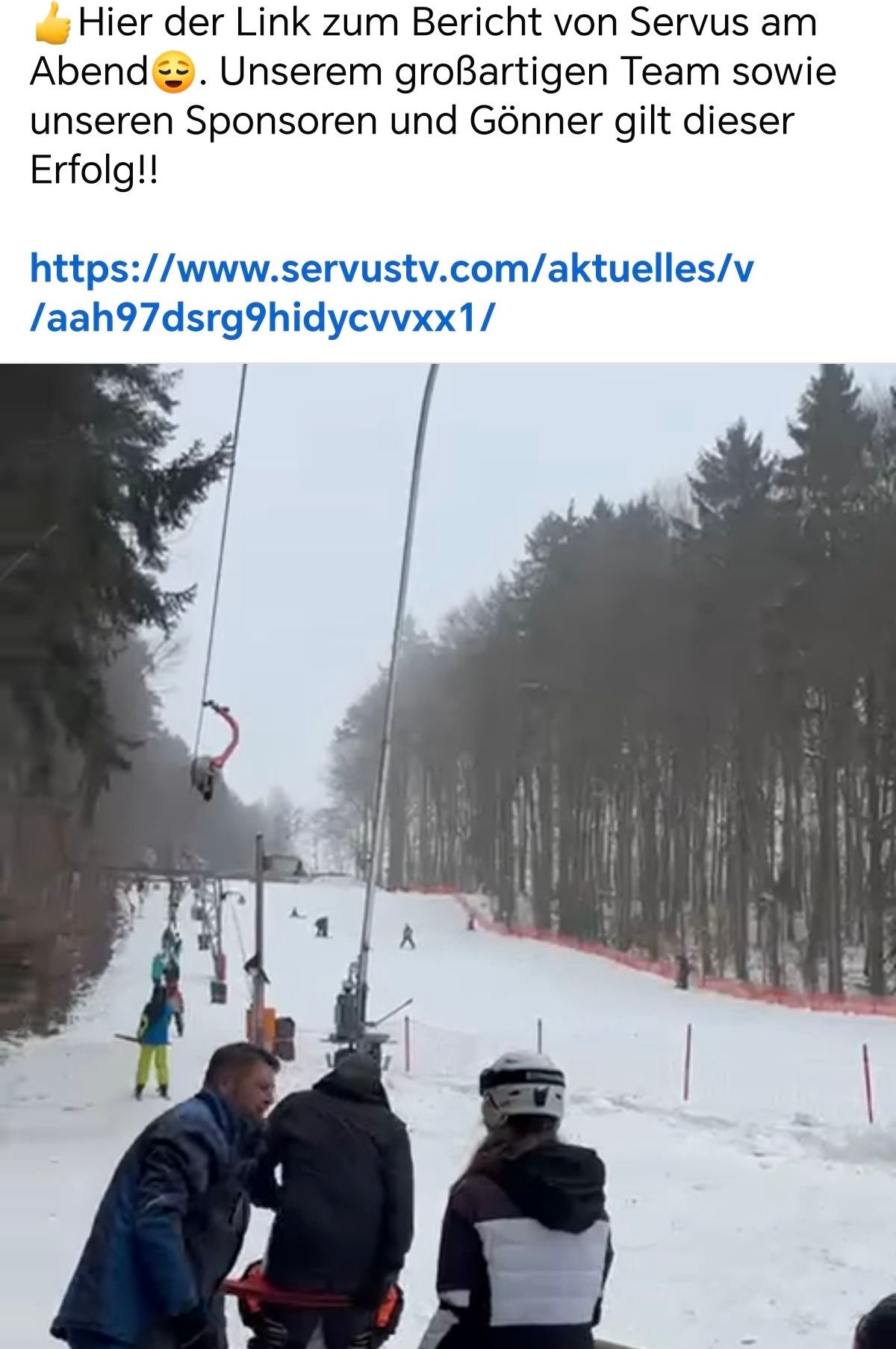Eine Skipiste mit Skifahrern und Stehenden. Es gibt Skilifte und Bäume entlang der Piste. Der Himmel ist bewölkt.