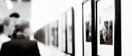 Ein monochromes Bild einer Person, die gerahmte Bilder an einer Wand betrachtet, verwaschener Fokus auf den Betrachter.