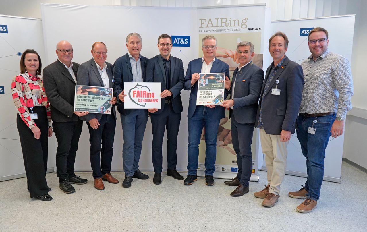 Eine Gruppe von Männern in formeller Kleidung steht in einer Reihe, hält Urkunden und lächelt. Der Mann in der Mitte hält eine Urkunde mit dem Wort FAIRing. Die Gruppe steht vor einem Banner mit dem FAIRing-Logo und Text.