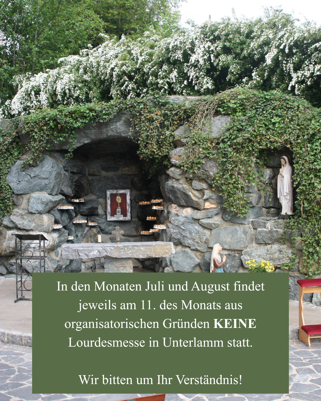 Ein steinerner Altar mit einer Statue der Maria und einem Kreuz, umgeben von Felsen und Grün. Eine Mitteilung am unteren Rand besagt, dass am 11. Juli und August keine Messe stattfinden wird.