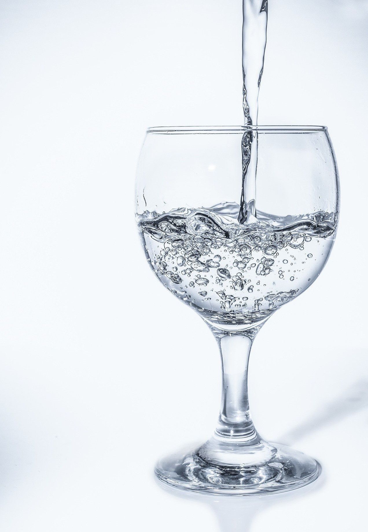 Wasser wird in ein Weinglas gegossen und erzeugt dabei Blasen und Wellen auf der Oberfläche.