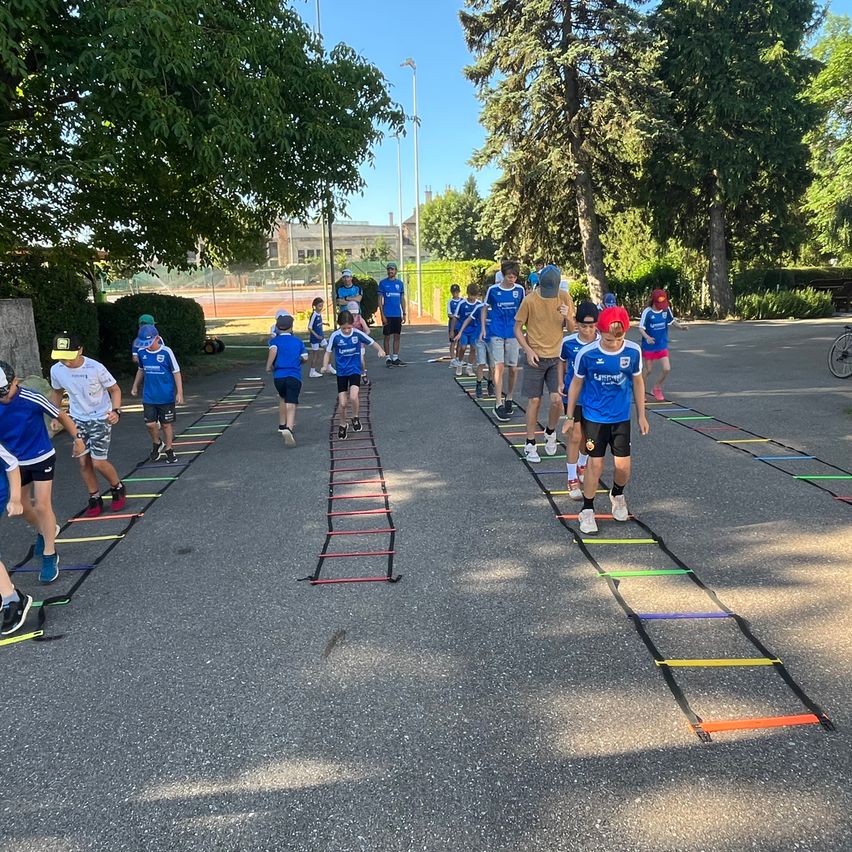 Eine Gruppe von Menschen in blauen Uniformen übt auf der Straße Beweglichkeitsübungen. Sie laufen auf und ab an den auf der Straße platzierten Leitern.