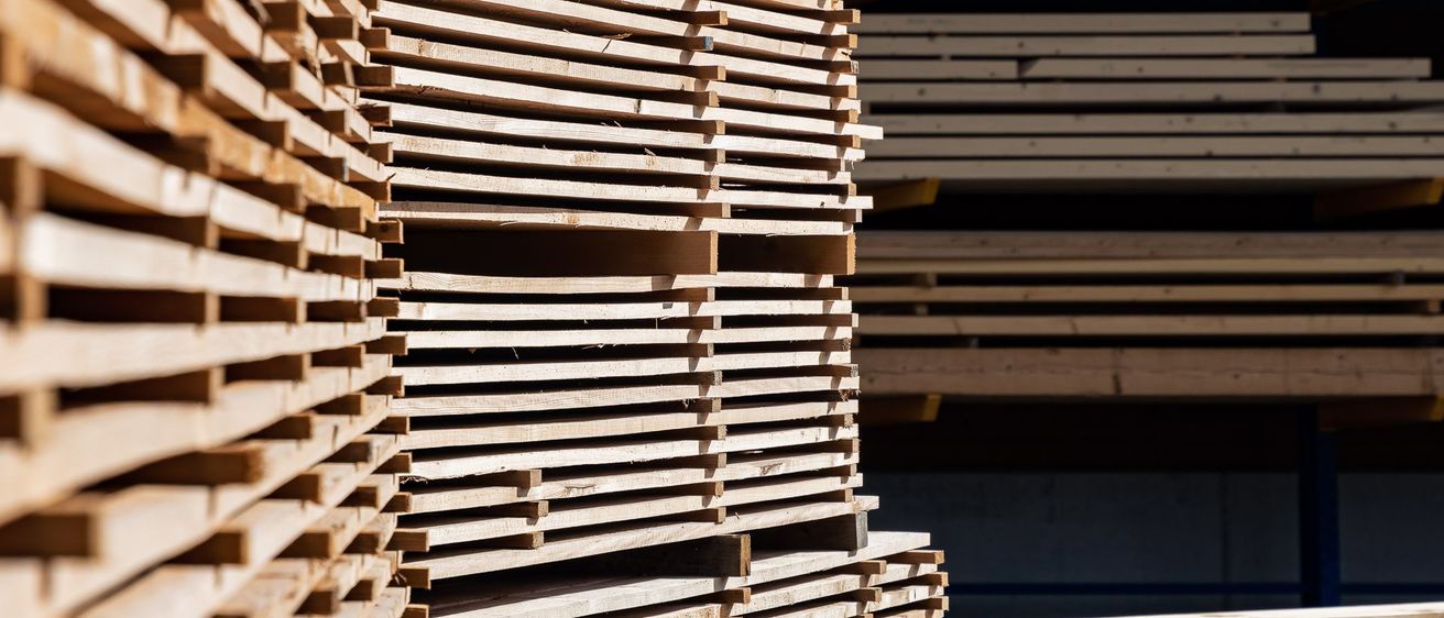 Eine Nahaufnahme von mehreren Stapeln hölzerner Bretter, die in Reihen angeordnet sind, wahrscheinlich in einem Lagerhaus.